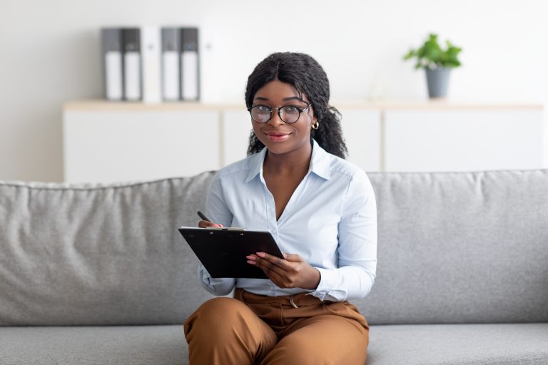 Smiling student sitting on couch with clipboard taking notes